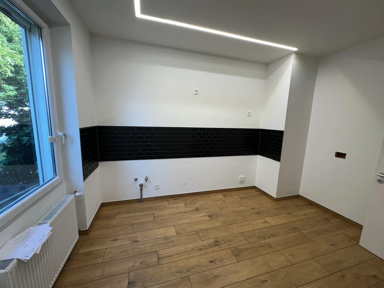 Küchenraum mit schwarzem Fliesenspiegel, Boden in Holzoptik und LED-Deckenbeleuchtung
