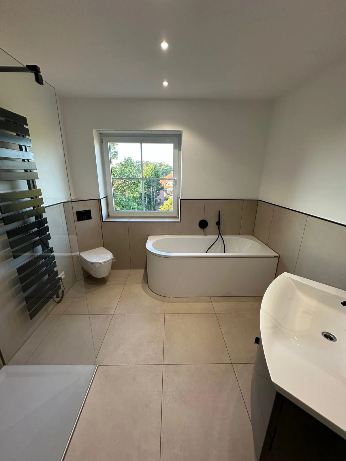Badezimmer mit Badewanne, separatem Duschbereich und großformatigen Bodenfliesen
