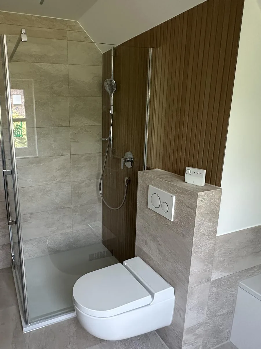 Duschbereich mit Glasabtrennung, Wandgestaltung in Holzoptik und WC-Vorwand
